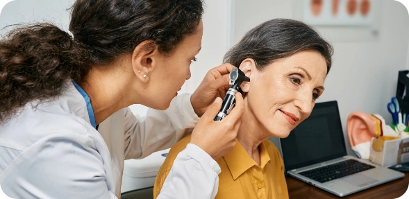 A doctor examining a woman's ears at an adult hearing services appointment.